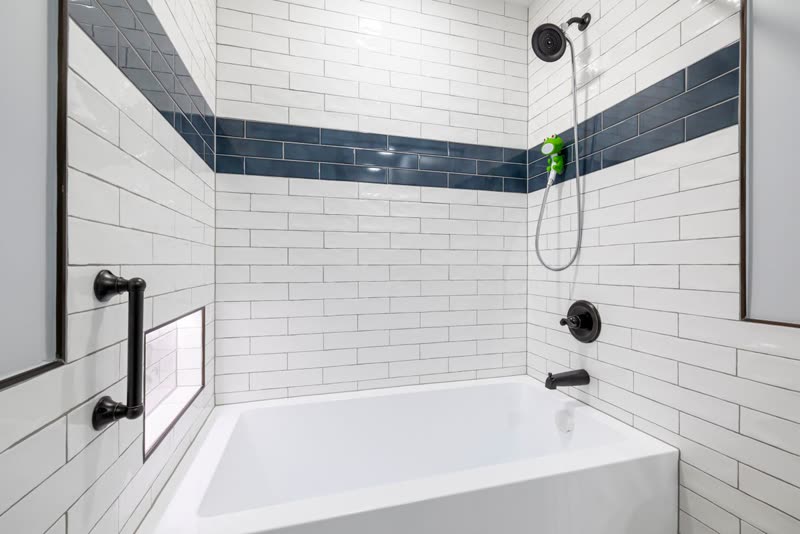 White subway tile with a blue accent band around a bathtub alcove
